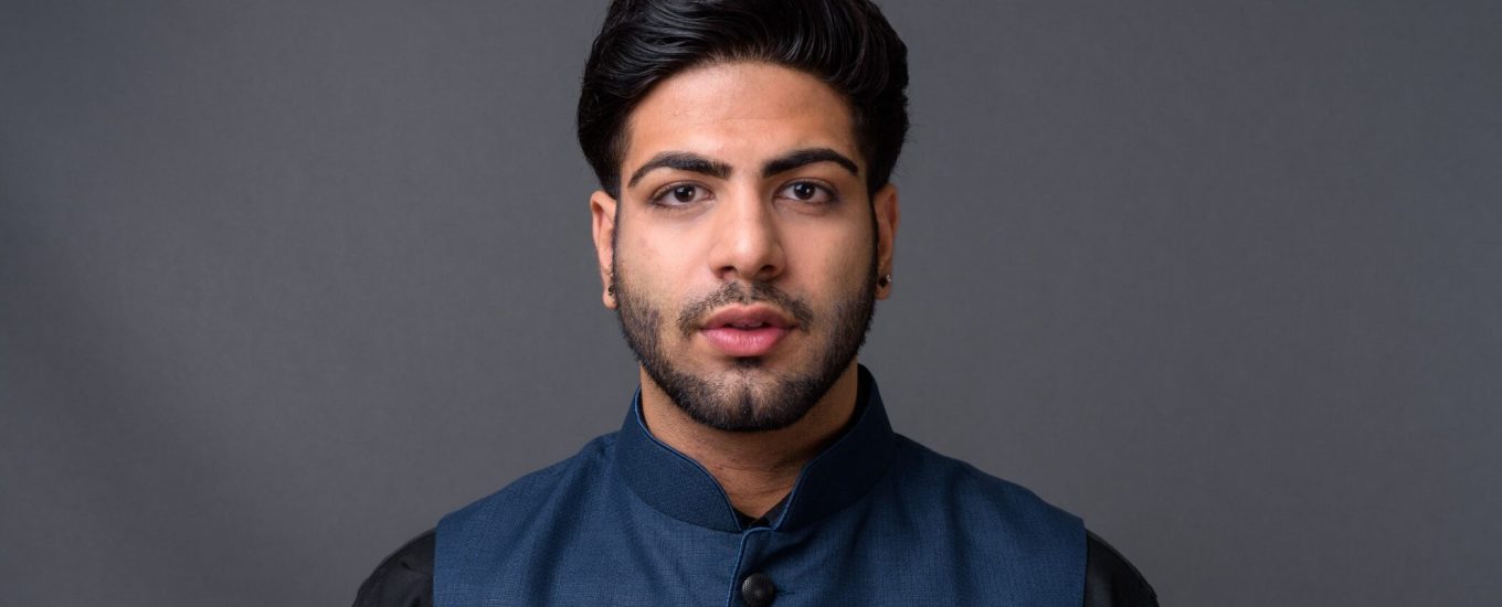 Studio shot of young handsome Indian businessman against gray background